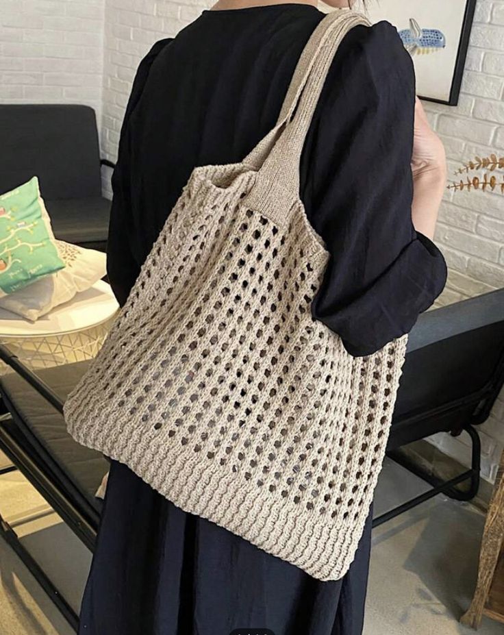 a woman carrying a crochet bag in her hands while standing next to a table