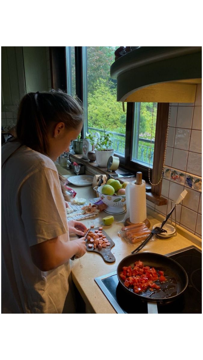 a woman is preparing food on the stove top in her kitchen with a large window