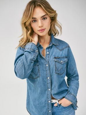 A WARDROBE STAPLE NO COWGIRL SHOULD GO WITHOUT No Western wardrobe would be complete without a classic snap shirt. Combining the 100% cotton denim you love with the clean and simple silhouette you can always depend on, the women's Wrangler Western snap denim shirt offers up vintage cowgirl style with some contemporary attitude. This long-sleeve snap shirt comes with many of the iconic Wrangler details you look for as signs of superior quality, including Western front and back yokes and genuine pearl snaps as well as snap flap pockets with our signature 'W' embroidery. Whether you wear it during the week or you save it for the weekend, you're guaranteed to get compliments anywhere you go. Now available in multiple washes to help you keep your closet stocked in style. Western Style Denim Blue Cotton Tops, Medium Wash Tops With Button Closure For Rodeo, Medium Wash Top With Button Closure For Rodeo, Distressed Long Sleeve Tops For Rodeo, Dark Wash Cotton Tops For Rodeo, Medium Wash Tops With Pockets For Rodeo, Long Sleeve Washed Tops For Rodeo, Rodeo Tops With Snap Buttons In Relaxed Fit, Classic Denim Tops For Rodeo