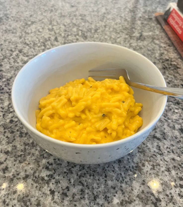 a white bowl filled with macaroni and cheese on top of a granite counter