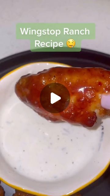 a person dipping sauce on top of a piece of food in a pan with chicken wings