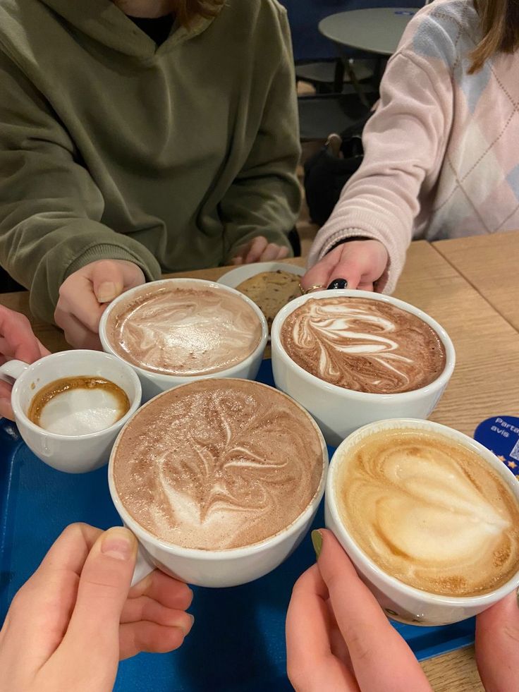 four people sitting at a table with cups of coffee in front of them and their hands on top of the mugs