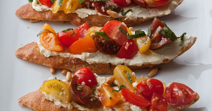 four pieces of bread with tomatoes, cheese and other toppings on them sitting on a white surface