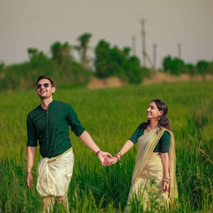 a man and woman holding hands walking through tall grass in the middle of a field