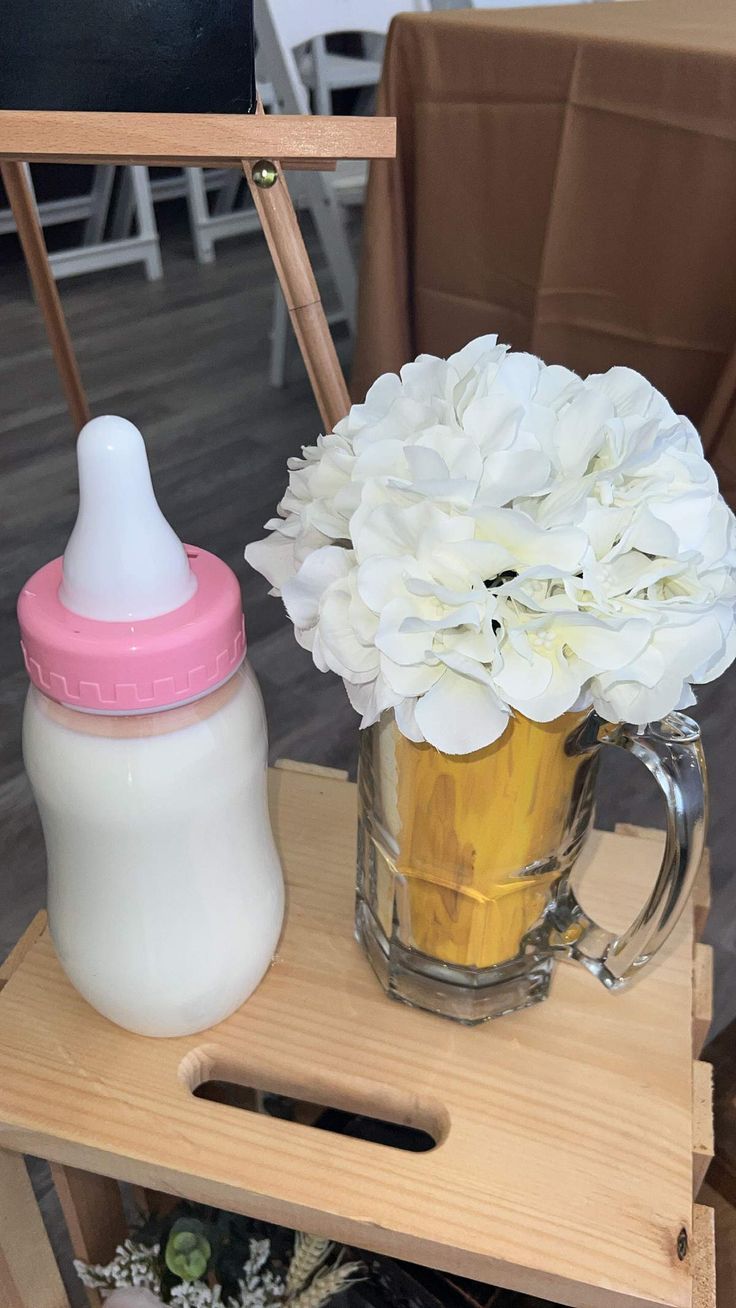 a baby bottle sitting on top of a wooden table next to a vase filled with flowers