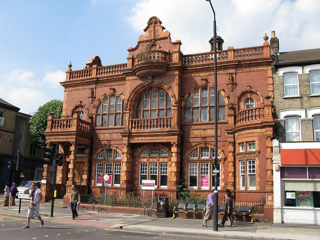 an old brick building on the corner of a street with people walking around it and buildings in the background