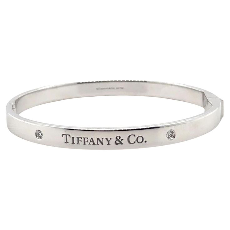 A Tiffany & Co. Diamond bangle, made of 18ct White Gold, and weighing 38.7 gm. Stamped: Tiffany & Co. AU 750. The bangle is set with 2 round, brilliant cut Diamonds, colour D-E and clarity VVS with a total weight of 0.10 ct. Metal: 18ct White Gold Carat: 0.10ct Colour: D-E Clarity: VVS Cut: Round Brilliant Weight: 38.7 grams Engravings/Markings: Signed Tiffany & Co. AU 750. Size/Measurement: Size Medium Current Condition: Excellent - Consistent with age and use. Accompanied by: This Tiffany & Co Tiffany And Co Diamond, Tiffany And Co Bracelet, Tiffany And Co, Diamond Bangle, Hinged Bangle, Brilliant Cut Diamond, Tiffany & Co., Round Brilliant, Hinges