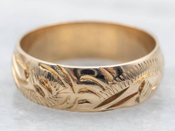 a gold wedding ring with an intricate design on the outside and inside, sitting on a white surface