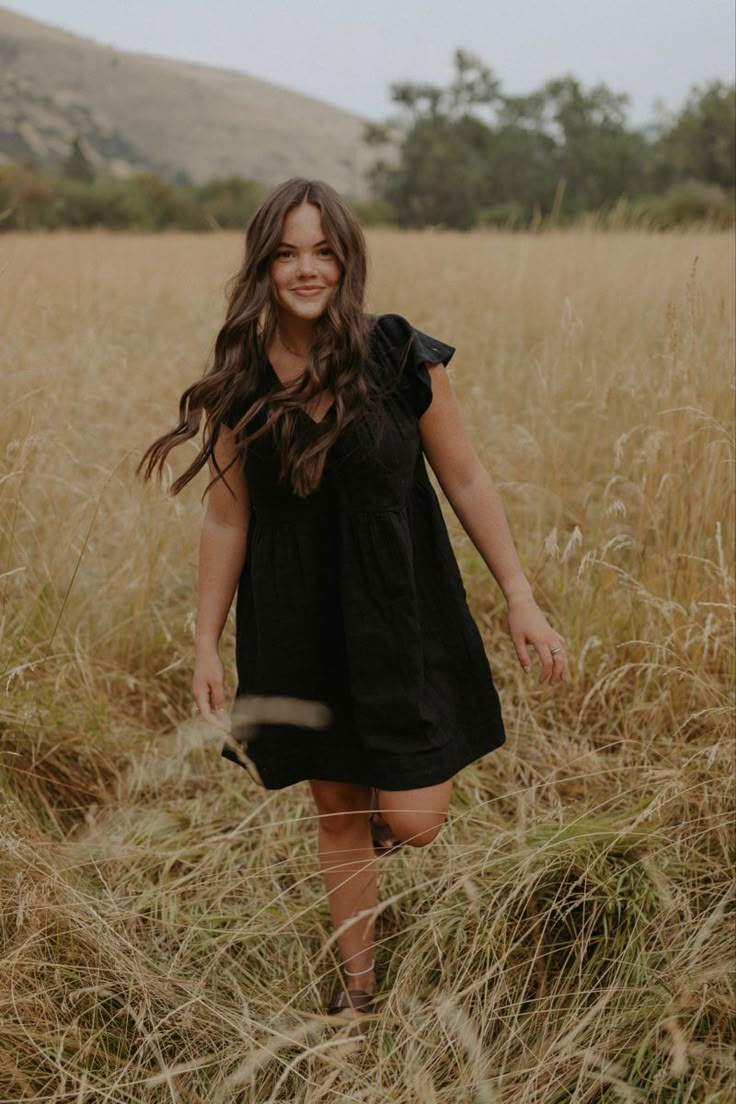 a girl in a black dress walking through tall grass