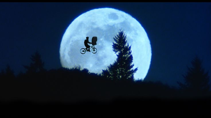 a full moon is seen in the sky with two people on bicycles flying over them