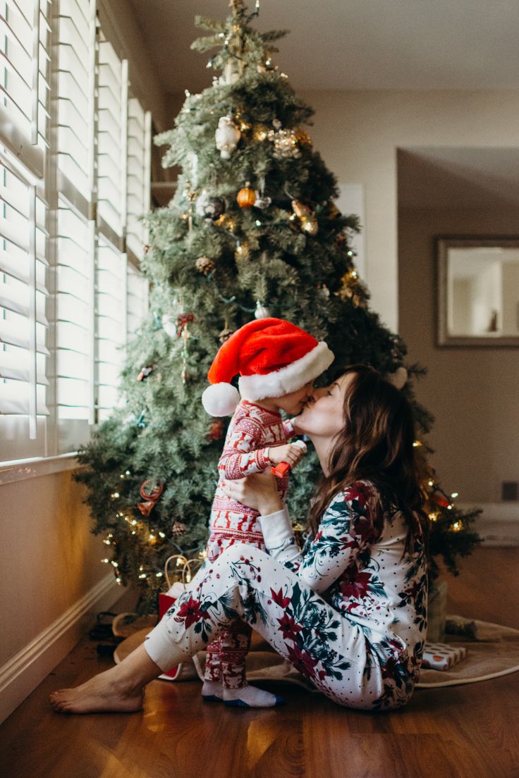 a woman sitting on the floor with her baby in front of a christmas tree