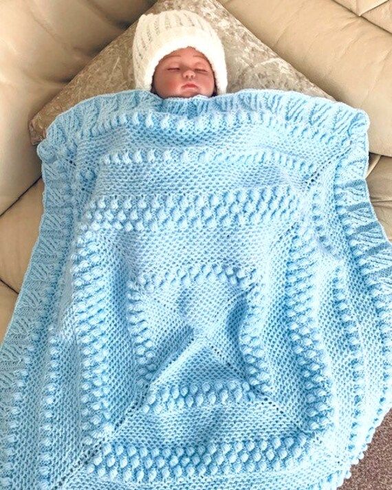 a baby wrapped up in a blue blanket on top of a couch next to a pillow