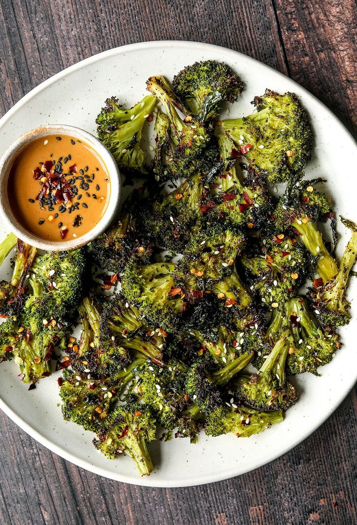 a white plate topped with broccoli covered in seasoning next to a small bowl of dipping sauce