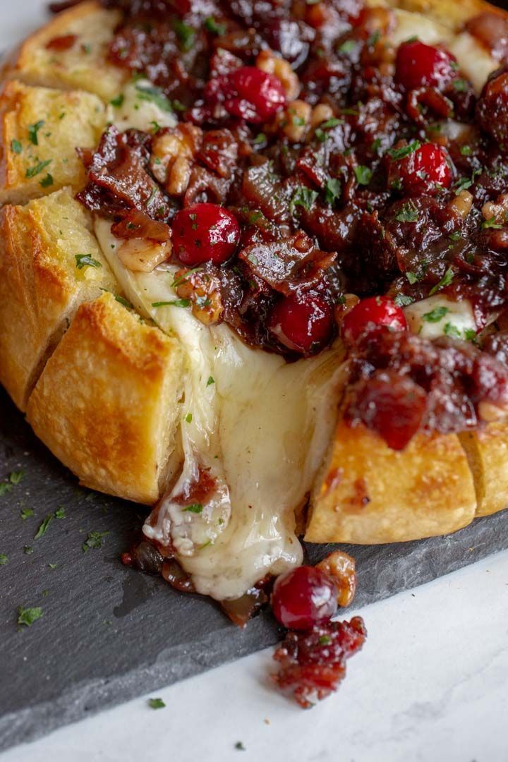 a cranberry bread pizza on a cutting board with cheese and herbs sprinkled all over it