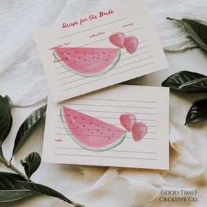 two cards with watermelon slices on them sitting next to some leaves and paper