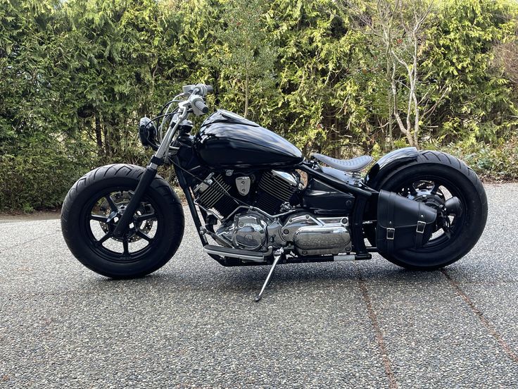 a black motorcycle parked on top of a parking lot next to some bushes and trees