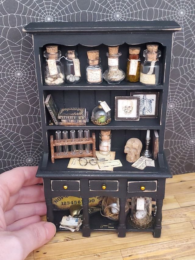 a hand holding a miniature book shelf with bottles and spices on it's shelves