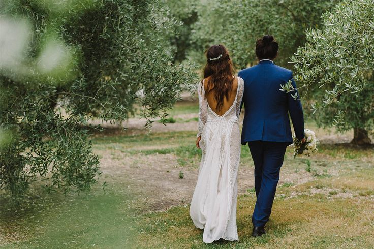 a bride and groom walking through an olive grove