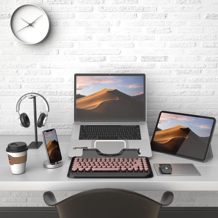 a desk with a laptop, phone and headphones on it in front of a white brick wall