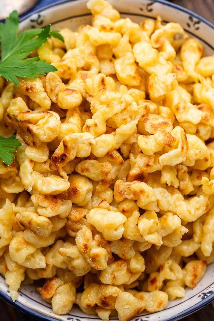 a bowl filled with macaroni and cheese on top of a wooden table next to parsley