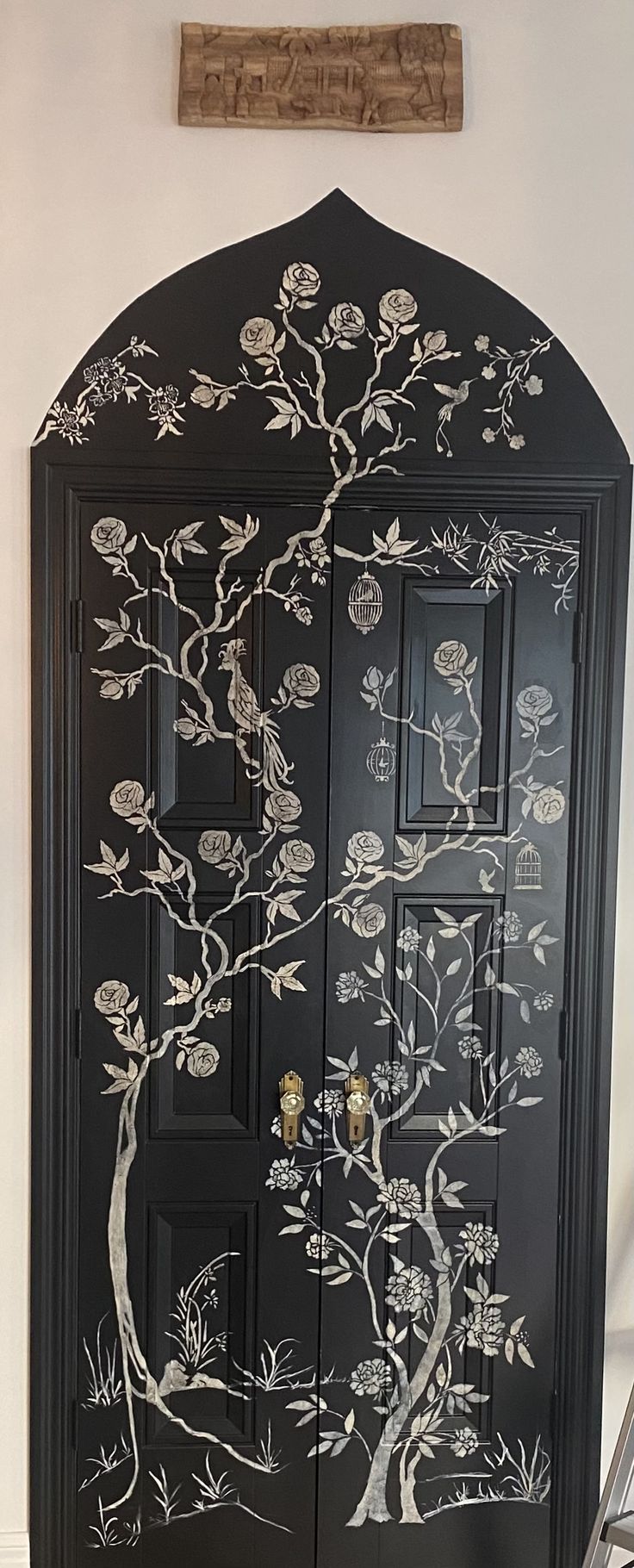 a black cabinet painted with white flowers and trees on it's doors is shown