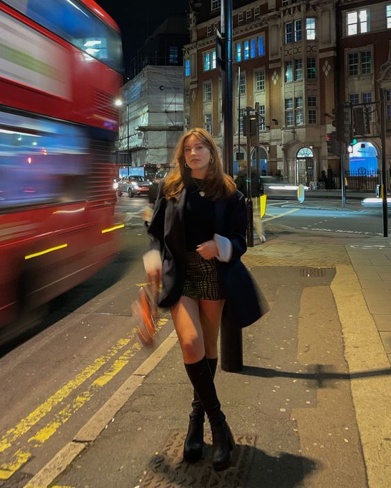 a woman is standing on the sidewalk in front of a red double - decker bus