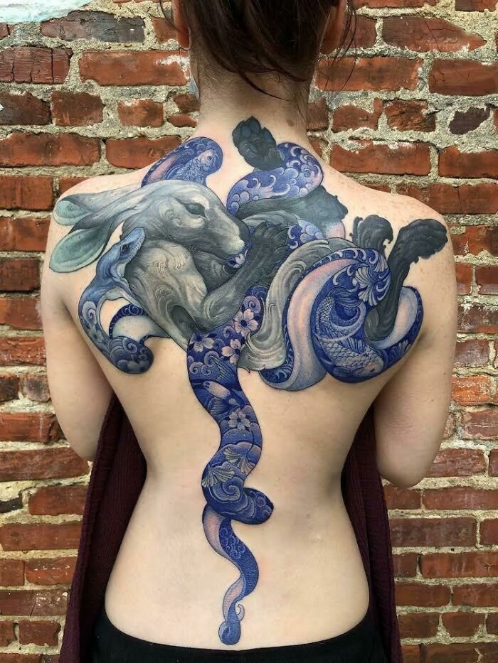 the back of a woman's body is covered in blue and white ink, with an intricate design on it