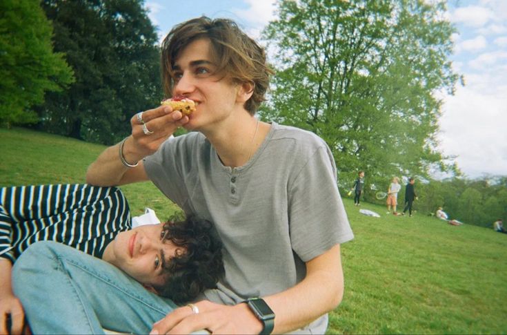 two young men sitting on the grass eating food