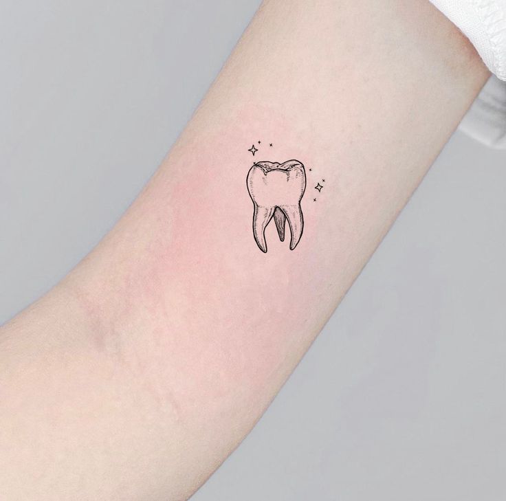 a small tooth tattoo on the left inner arm, with stars around it and an arrow in the middle