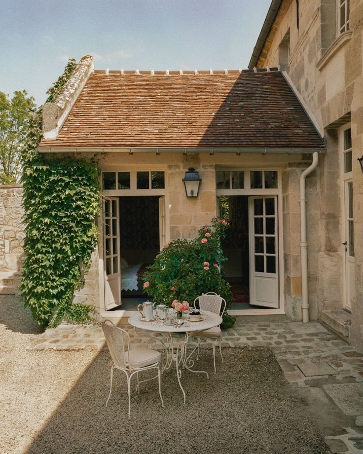 an outdoor table and chairs in front of a stone building with ivy growing on it