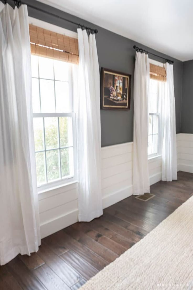 an empty bedroom with wood floors and white curtains