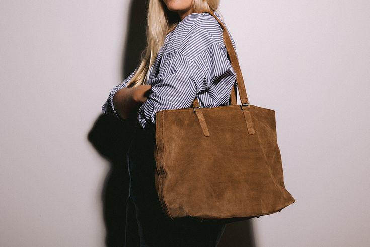 Introducing our Suede Tote: The Perfect Blend of Style and Functionality I designed this bag out of a need for a way to carry my laptop as the weather changes. I fell in love with this gorgeous caramel suede when I visited the tannery in Nairobi last year and knew it would be so perfect for fall. It's the perfect brown that feels golden and rich against black and is the perfect neutral tying together the color tones in your fall wardrobe. I like to wear my Sling Bag even while carrying The Tote Everyday Suede Bags With Leather Lining, Classic Everyday Suede Shoulder Bag, Classic Everyday Bags With Suede Lining, Classic Bags With Suede Lining For Everyday Use, Everyday Suede Satchel With Suede Lining, Suede Satchel With Suede Lining For Travel, Travel Tote Bag With Suede Lining, Cognac Suede Bag For Daily Use, Brown Suede Travel Bag