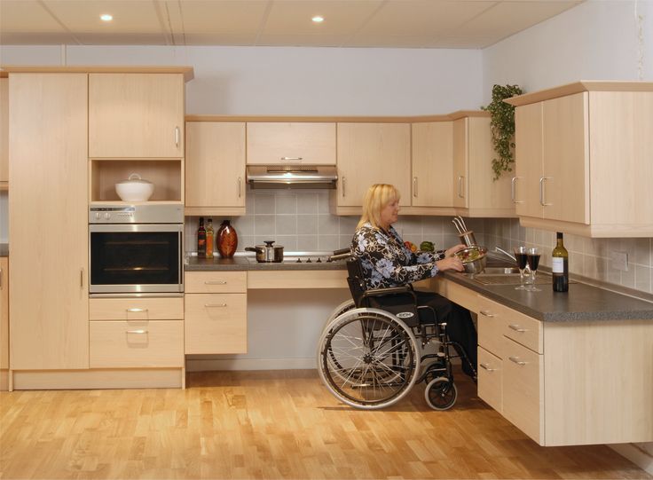 a woman in a wheel chair is at the kitchen counter with an oven, sink and dishwasher