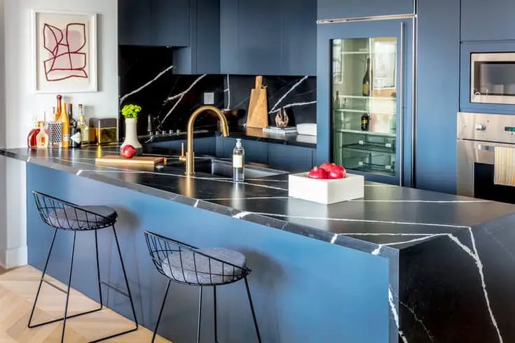 a kitchen with blue cabinets and marble counter tops, two bar stools next to the island