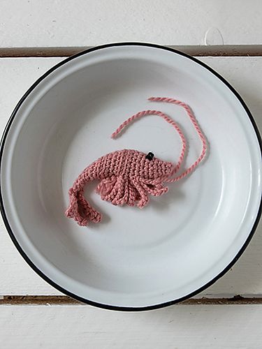 a crocheted pink rat on a white plate with black trimmings, sitting on a wooden surface