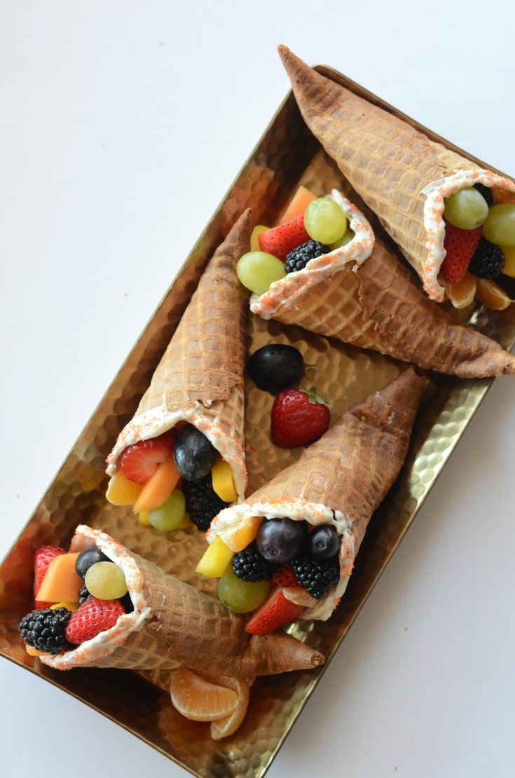 some fruit is wrapped in waffle cones on a plate with grapes, strawberries, and kiwis