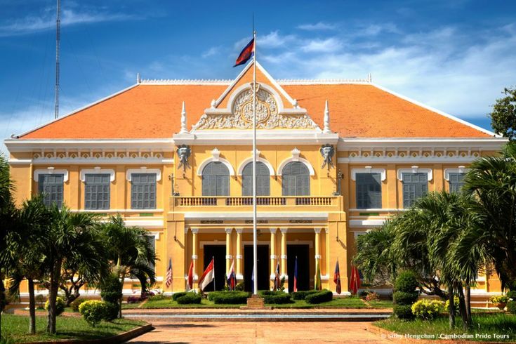 a large yellow building with two flags flying in front of it and palm trees around the entrance