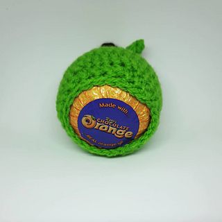 a green crochet ball with an orange label on it's end sitting on a white surface