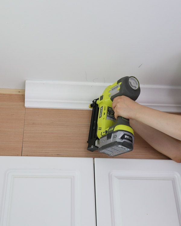 a person using a power drill to attach the door trim on a white cabinet with wood flooring