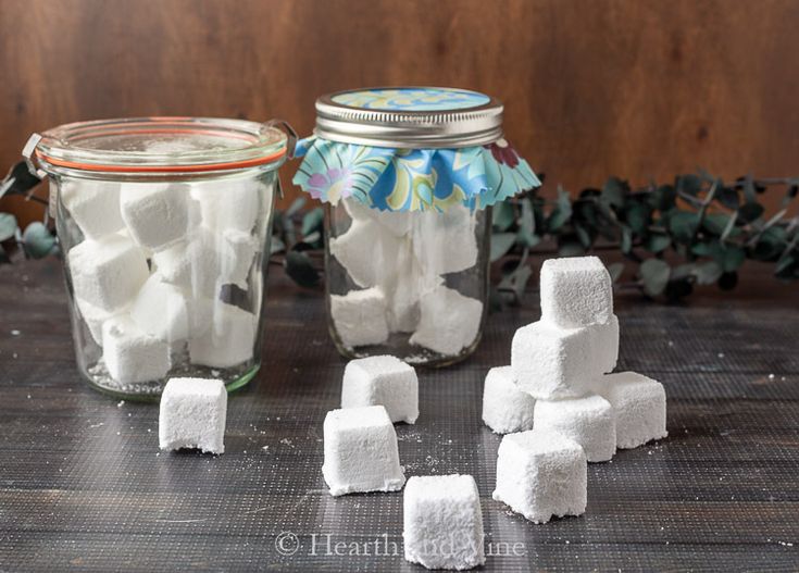 marshmallows are sitting on a table next to a glass jar full of sugar