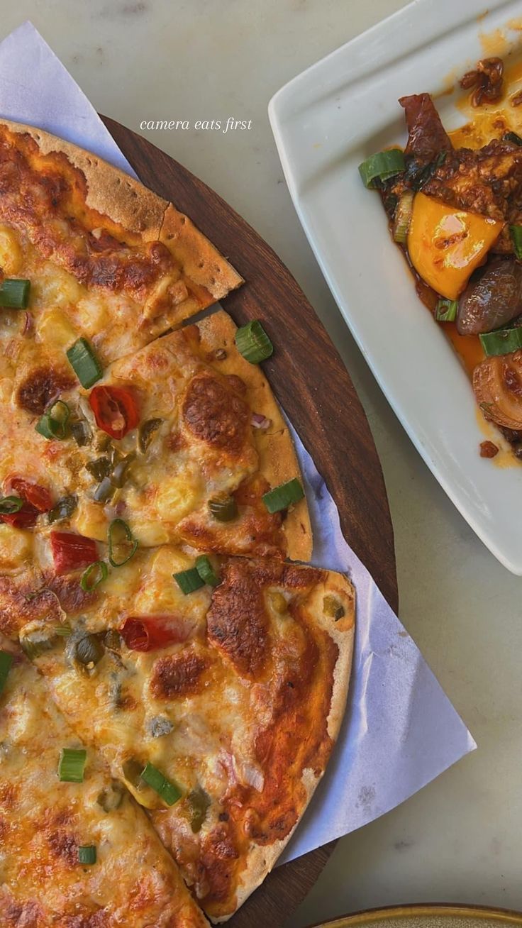 two pizzas sitting on top of a table next to a plate filled with food