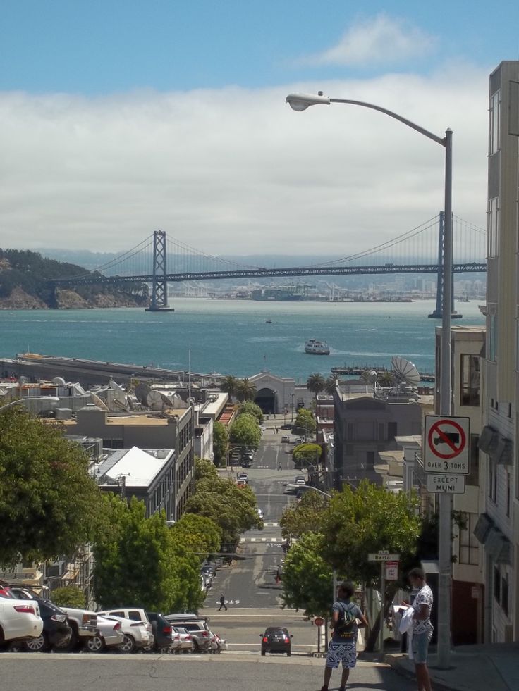 a view of the bay bridge in san francisco, california with people walking on the sidewalk