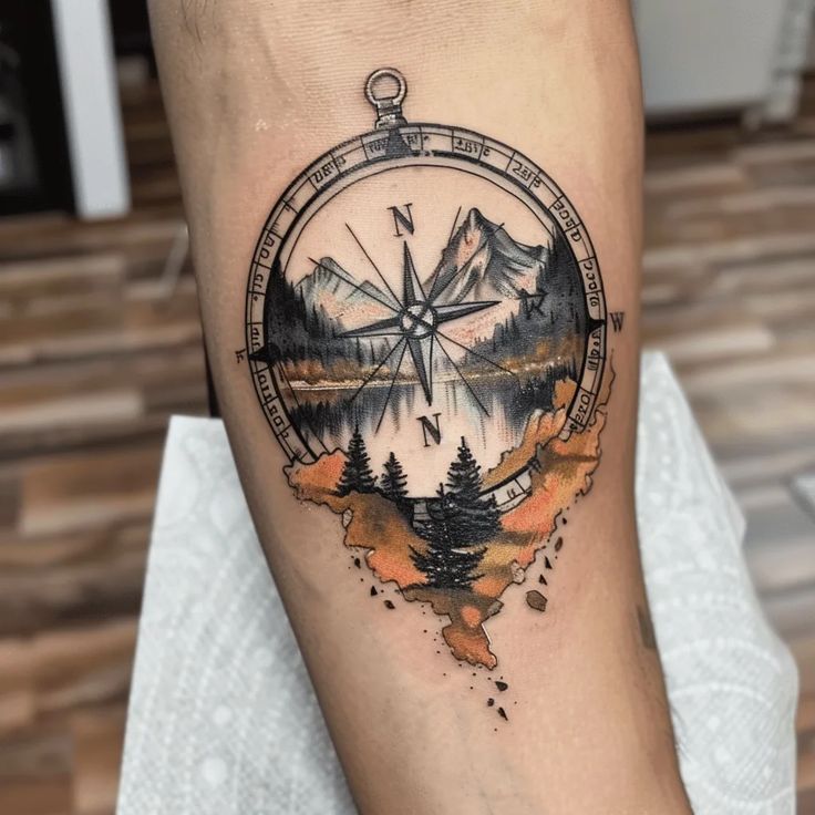 a compass tattoo on the leg of a person with mountains and trees in the background