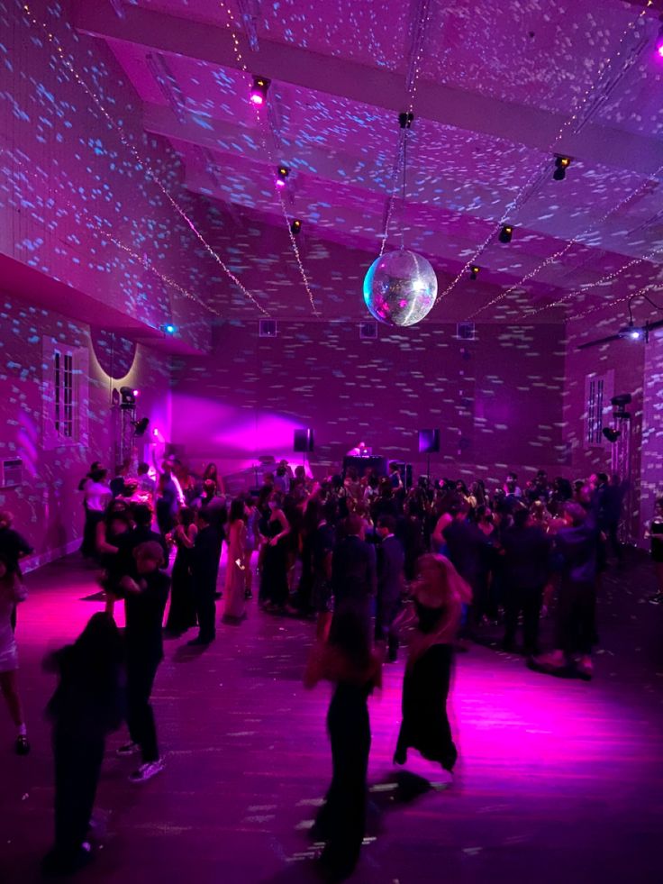 a group of people dancing in a room with purple lighting and disco balls on the ceiling