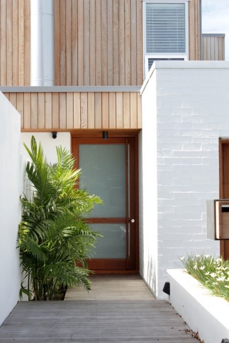 an entrance to a house with wooden sidings and plants in the foreground, next to a white wall