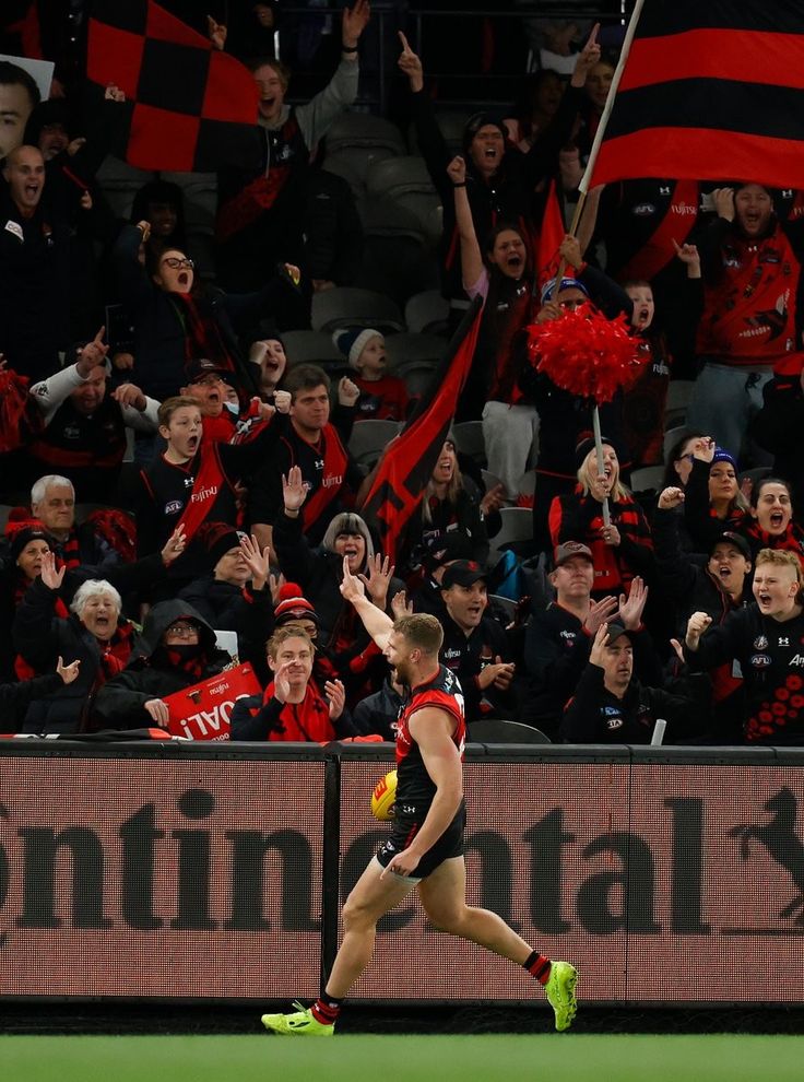 a soccer player is running on the field with fans in the stands behind him and his hand up