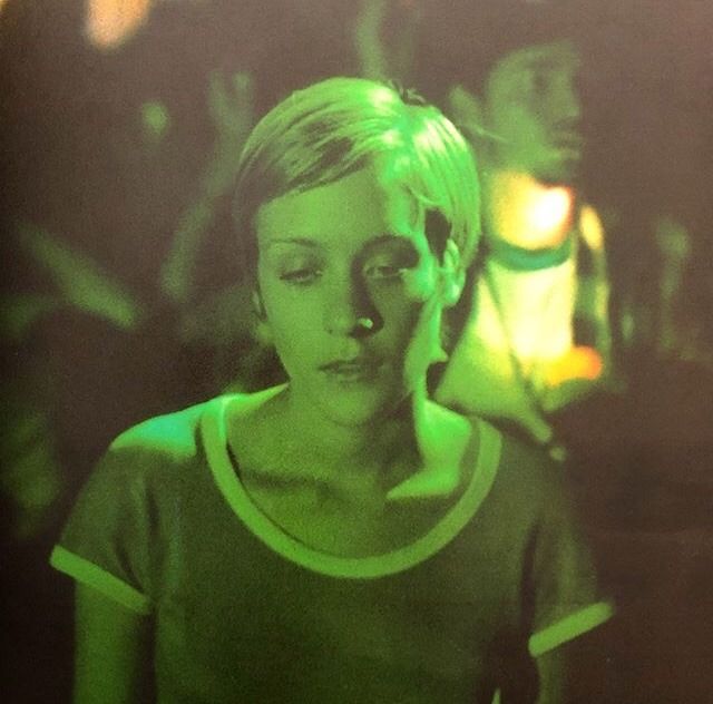 a young woman standing in front of a group of people with green light on her face