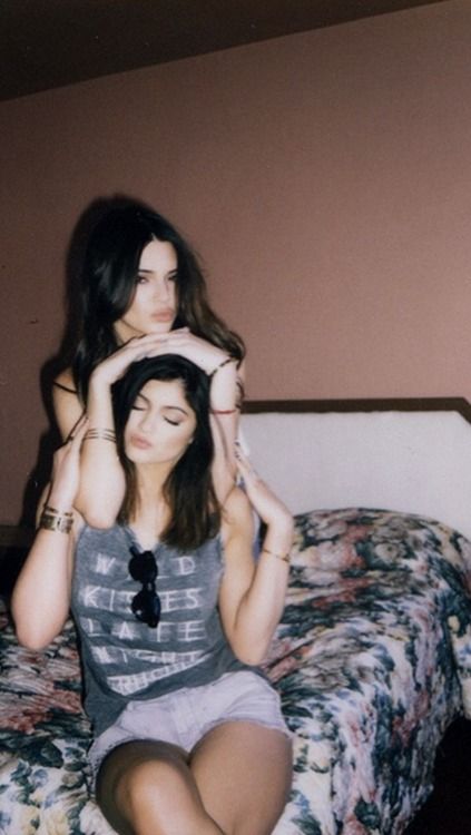 two women sitting on a bed with their arms around each other's head,