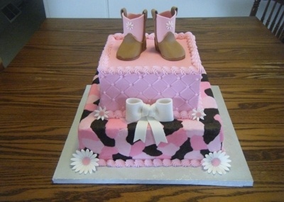 a pink and black cake with white flowers on the bottom, boots in the middle