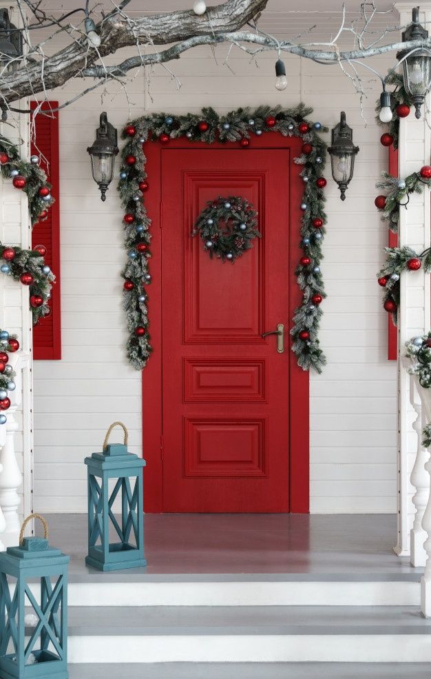 a red front door decorated for christmas with wreaths and lanterns